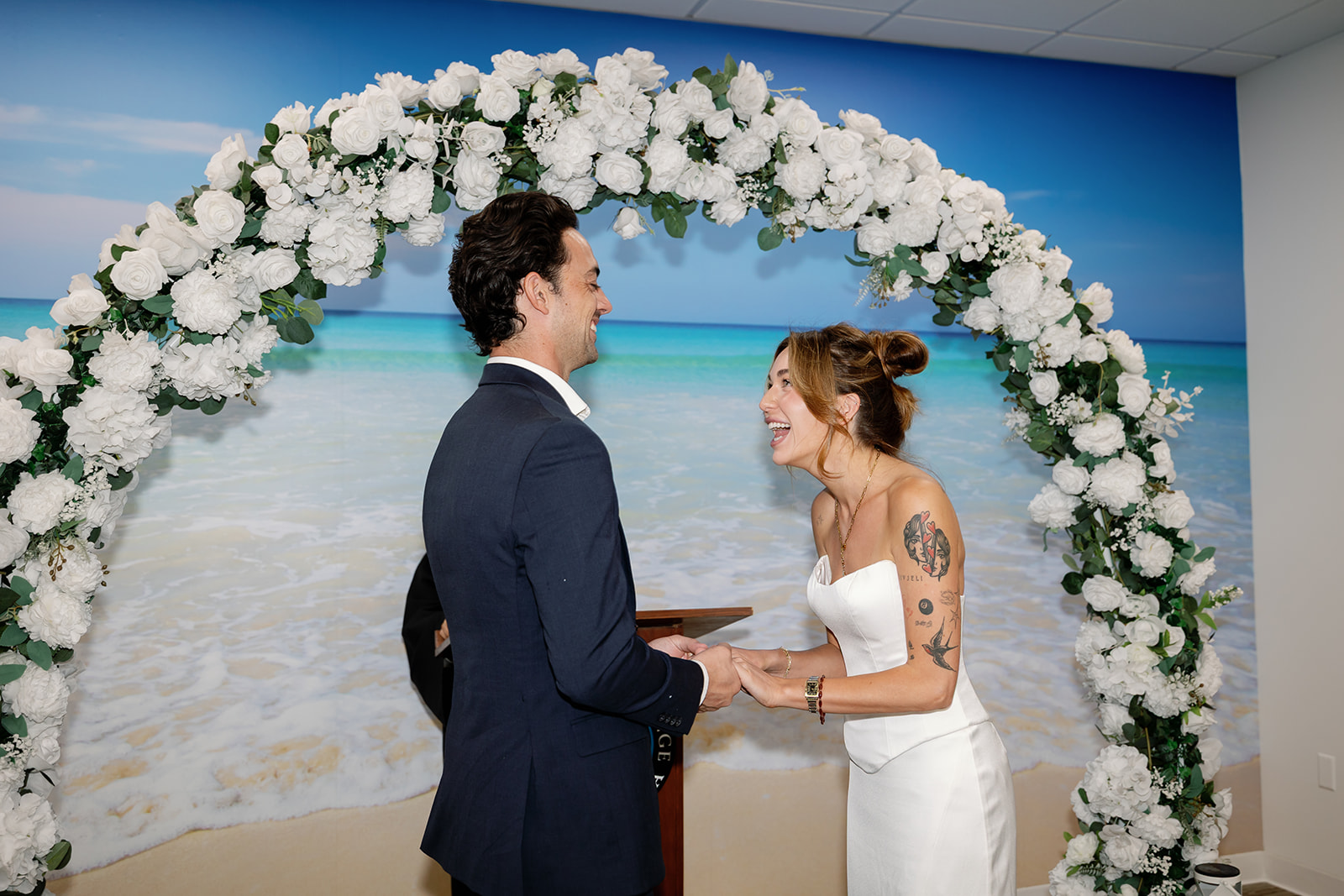 Bride and groom holding hands and laughing under a floral arch during Laguna Hills Civic Center elopement ceremony.
