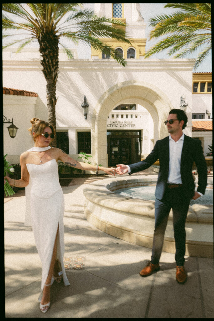 35mm film portrait of a bride and groom holding hands in front of Laguna Hills Civic Center during elopement portraits.