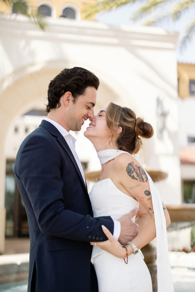 Close up photo of a bride and groom touching noses outside of a courthouse.