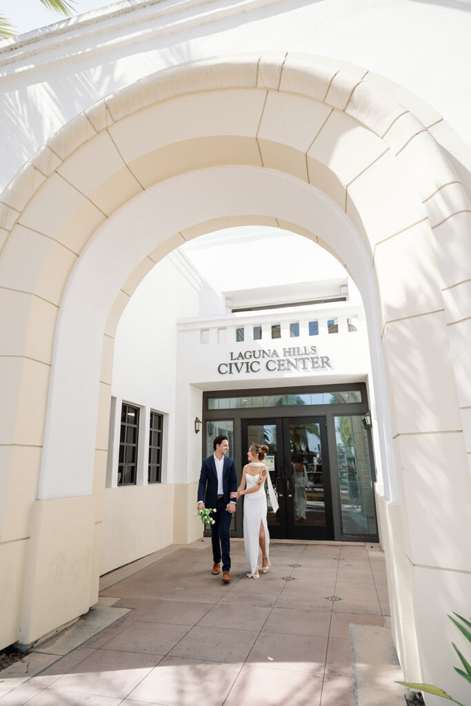 Bride and groom holding hands in front of Laguna Hills Civic Center during elopement portraits.