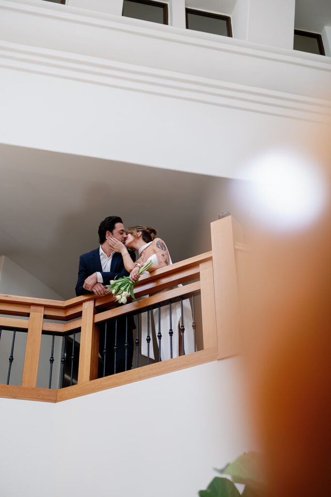 Bride and groom kissing on balcony inside Laguna Hills Civic Center during elopement portraits.