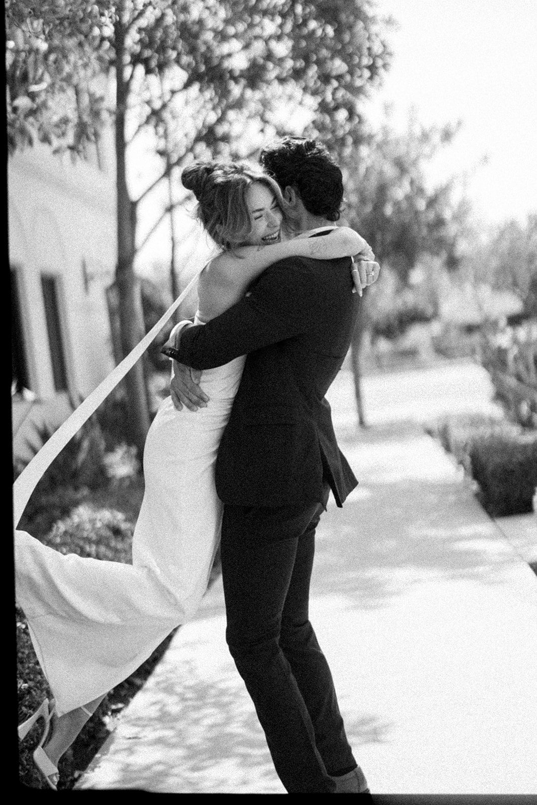 Black and white 35mm film portrait of a groom lifting and spinning his bride around outside of Laguna Hills Civic Center in Orange County, CA.