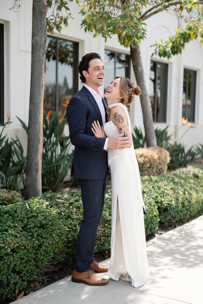 Bride and groom laughing together outside Laguna Hills Civic Center during elopement portraits.