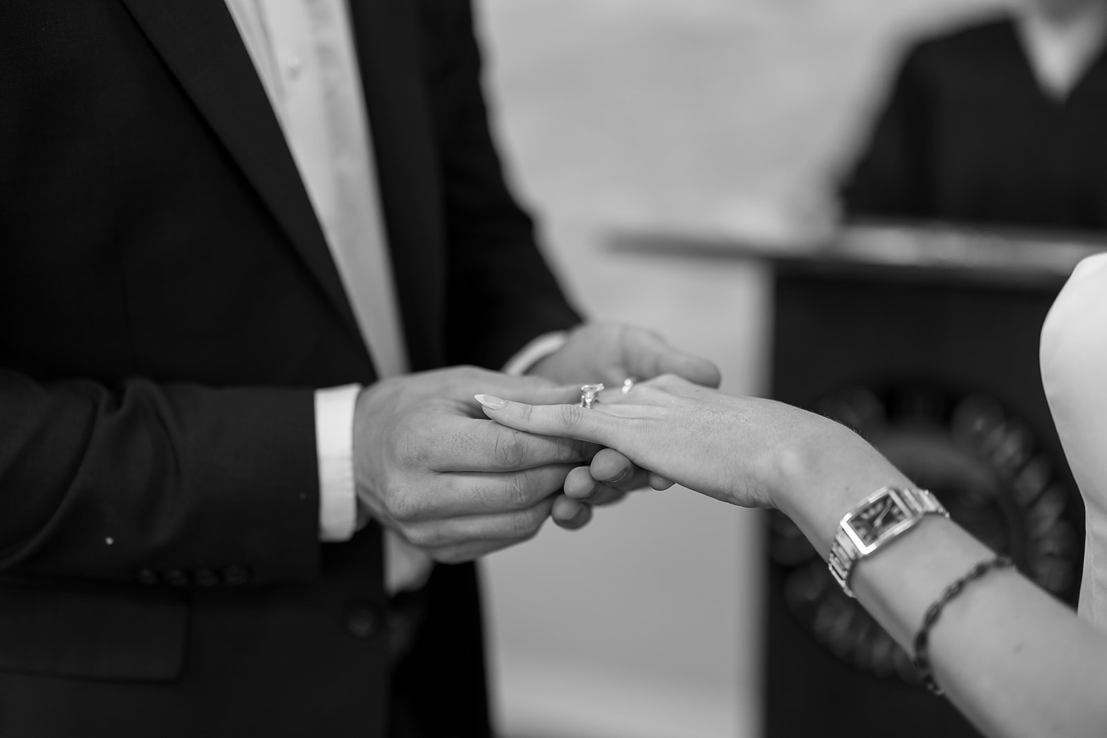 Close up black and white photo of the groom placing the ring on his brides finger during their ceremony.
