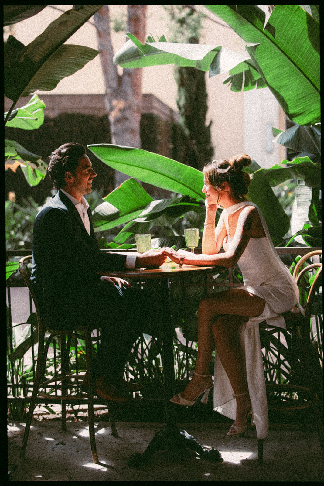 35mm film photo of a bride and groom holding hands across table surrounded by tropical greenery at Habana in Irvine Spectrum after elopement.