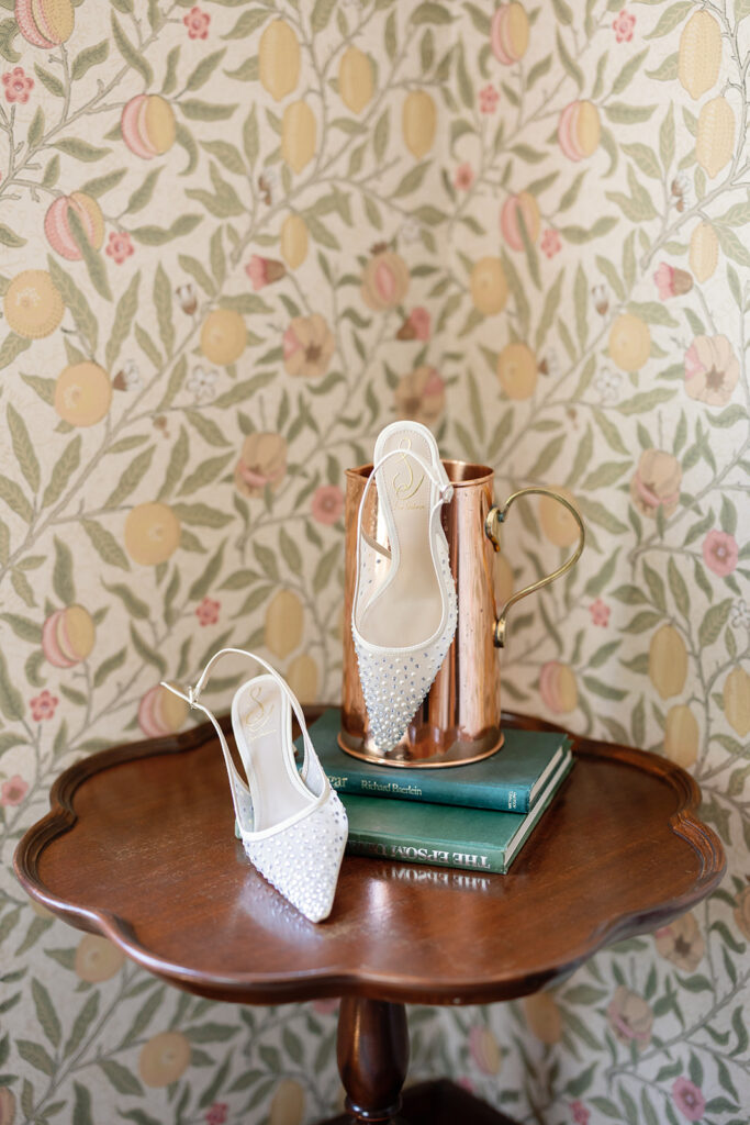 Bridal shoes styled on table with books and copper mug at Swanner House wedding.