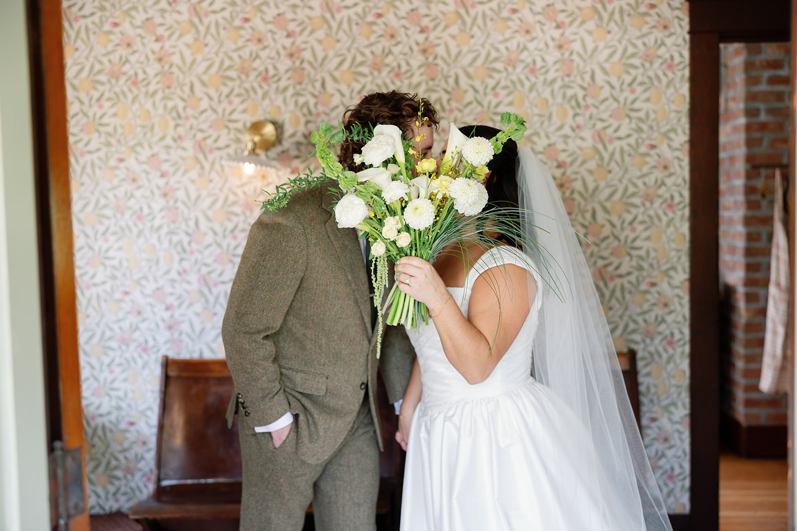 Couple kissing with a bouquet in front of wallpaper at Swanner House wedding.