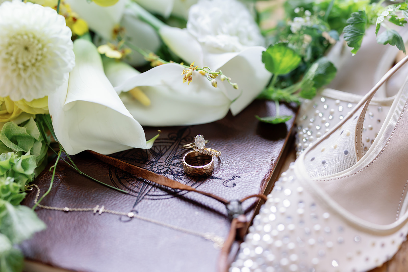Wide shot of wedding details including florals, rings, shoes, and a necklace. 