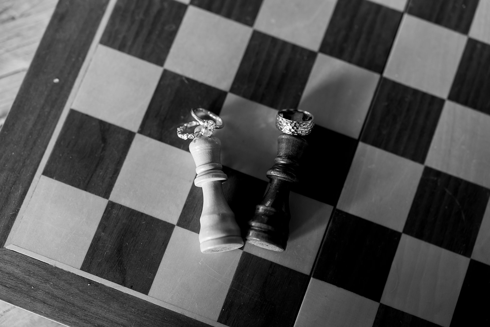 Black and white wedding detail shot with two chess pieces, wedding rings, and a wedding band. 