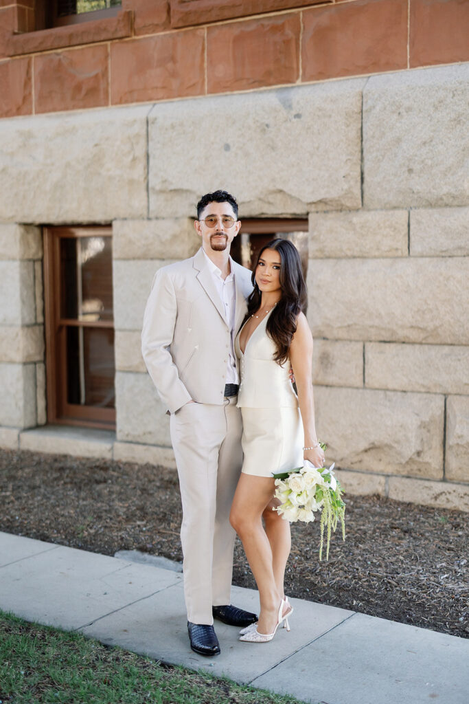 Bride and groom posing on a sidewalk outside of Old Orange County Courthouse in Santa Ana, California.