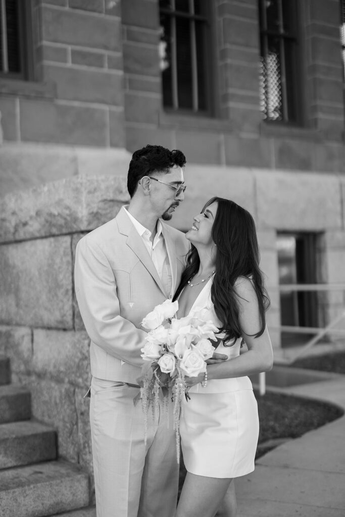 Black and white portrait of a bride and groom smiling at each other outdoors.