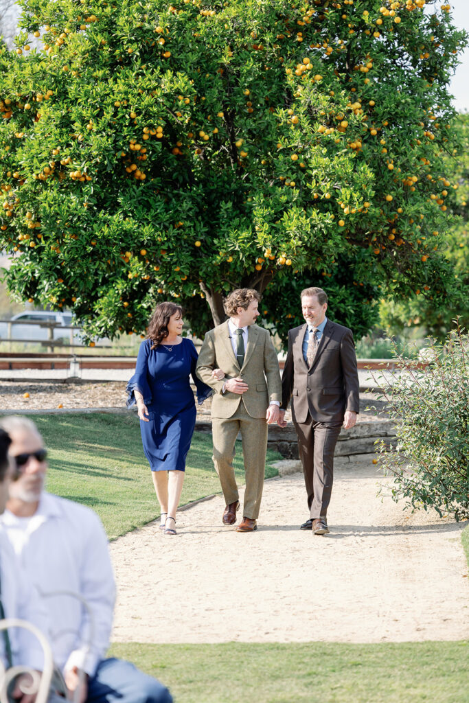 Groom walking with parents under orange trees at Swanner House wedding.