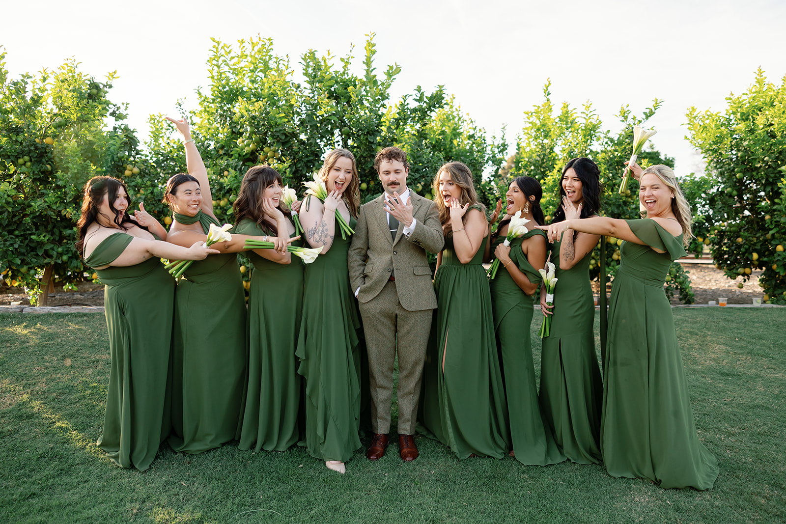 Groom with bridesmaids in green dresses posing playfully.