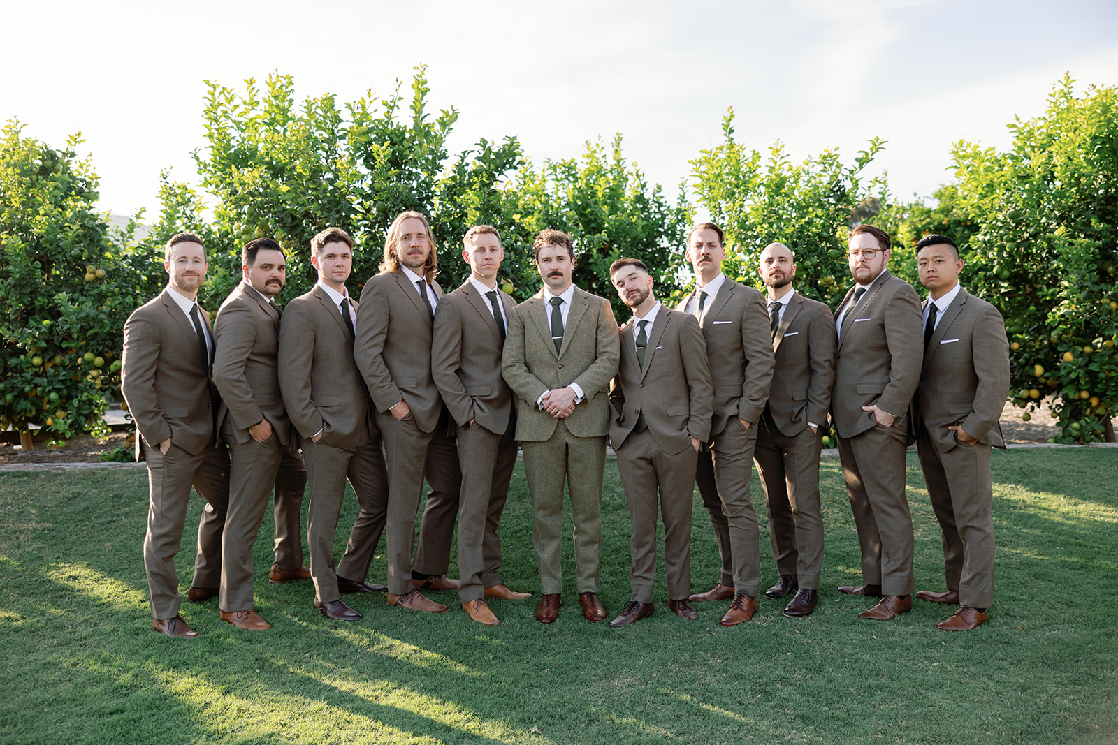 Groom with groomsmen posing in front of citrus trees at Swanner House wedding in San Juan Capistrano.