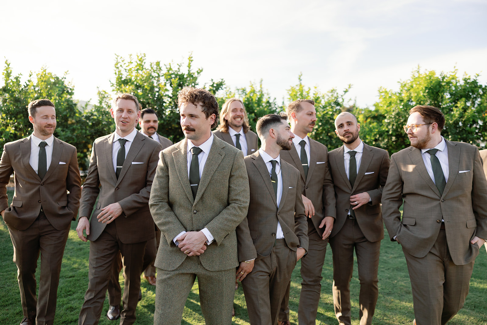 Groom with groomsmen walking in front of citrus trees at Swanner House wedding in San Juan Capistrano.