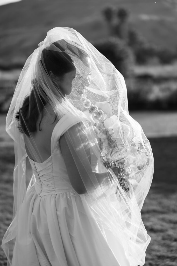 Black and white portrait of a bride posing under her veil with her bouquet at golden hour. 