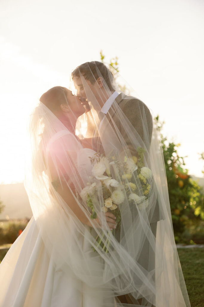 Bride and groom kissing under veil at sunset at Swanner House wedding in San Juan Capistrano.