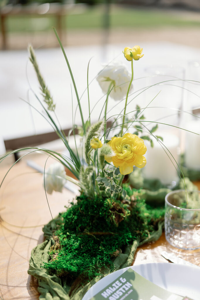 Outdoor reception table with moss runner and yellow floral centerpiece.