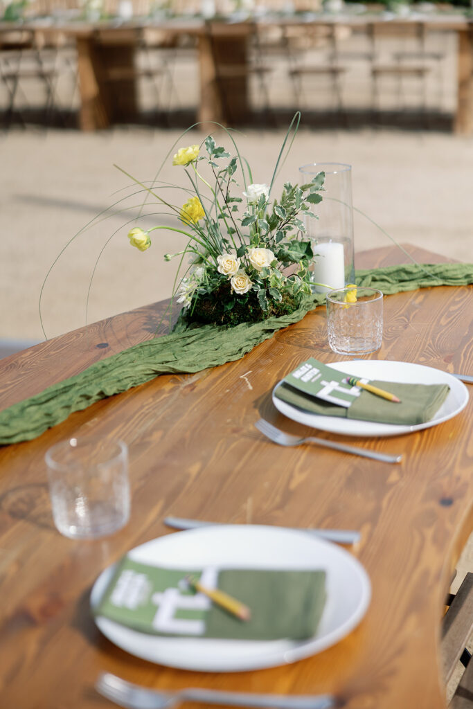 Outdoor reception table with moss runner and yellow floral centerpiece.