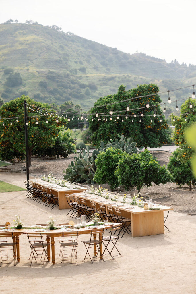 Reception space with long wooden tables, checkered dance floor, and citrus groves at a Swanner House wedding in San Juan Capistrano.