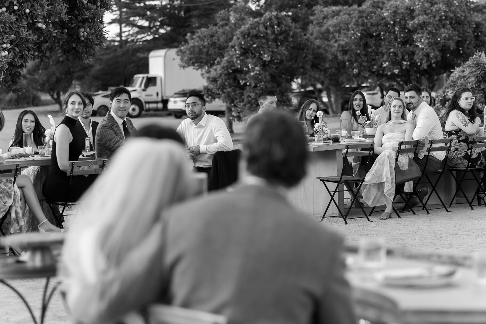 Black and white photo of a bride and groom listening to wedding reception speeches.