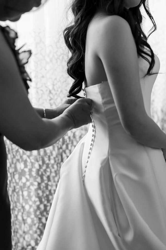 Black and white photo of the brides mother buttoning up her dress.