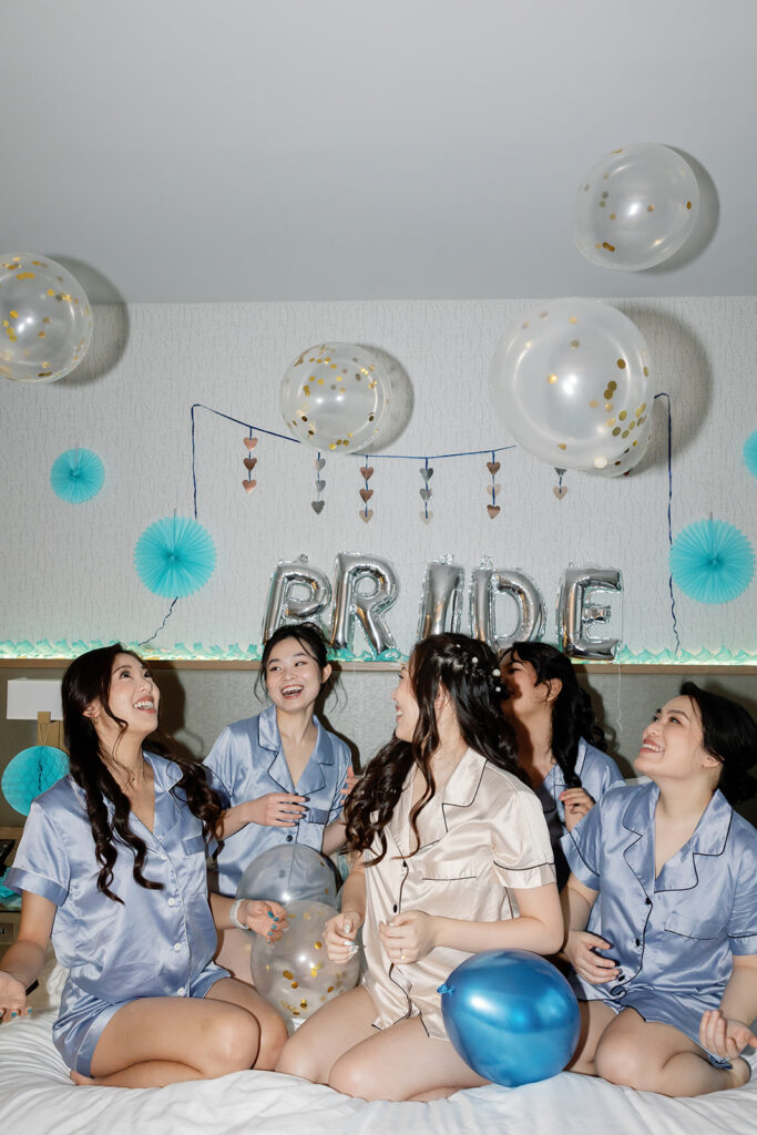 Bride and bridesmaids posing on a bed in their pajamas with balloons overhead as she gets ready.