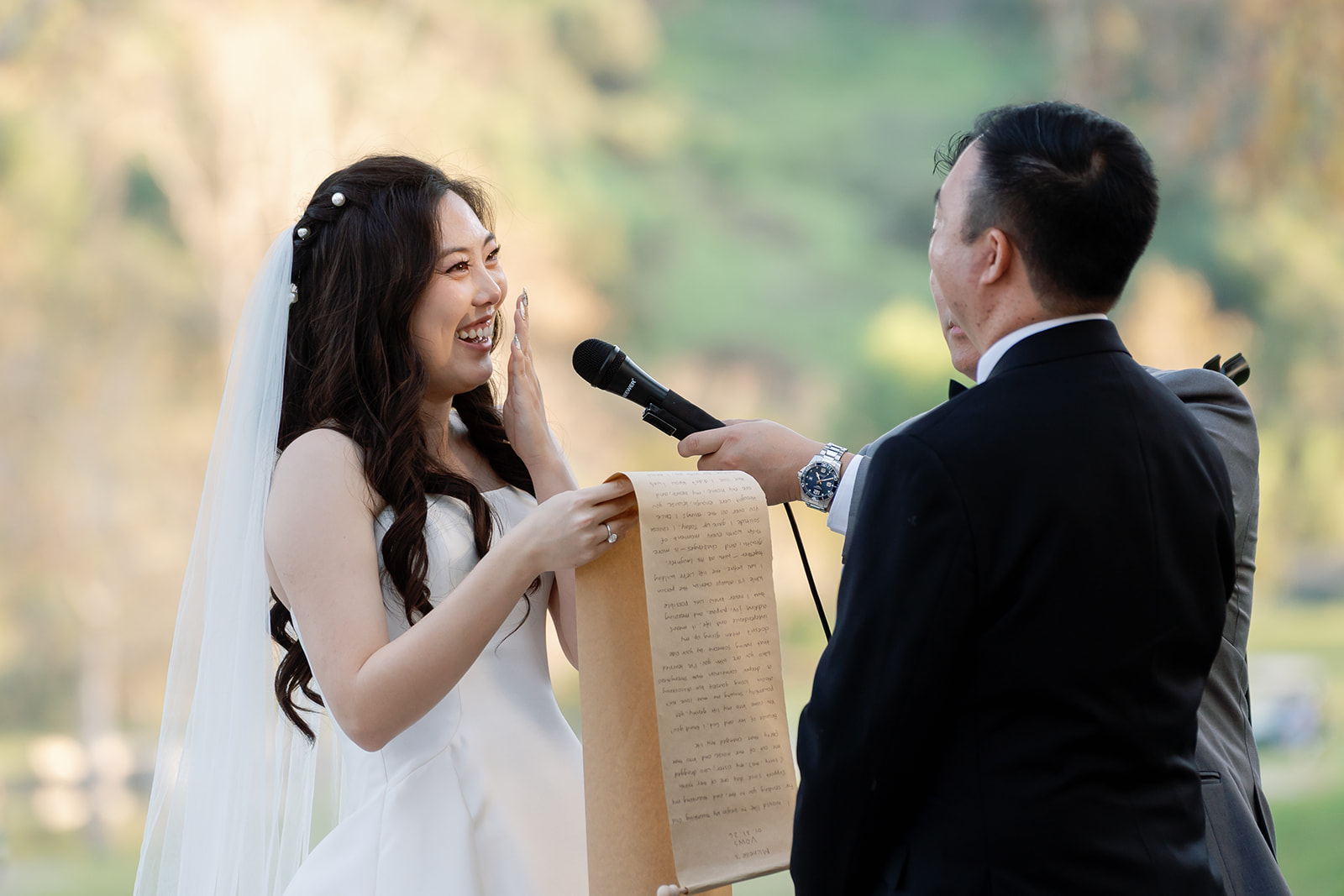 Bride laughing as she reads her vows to the groom from a long scroll. 