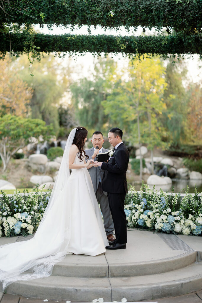 Bride putting a ring on the grooms finger during their outdoor Coyote Hills Golf Course wedding.