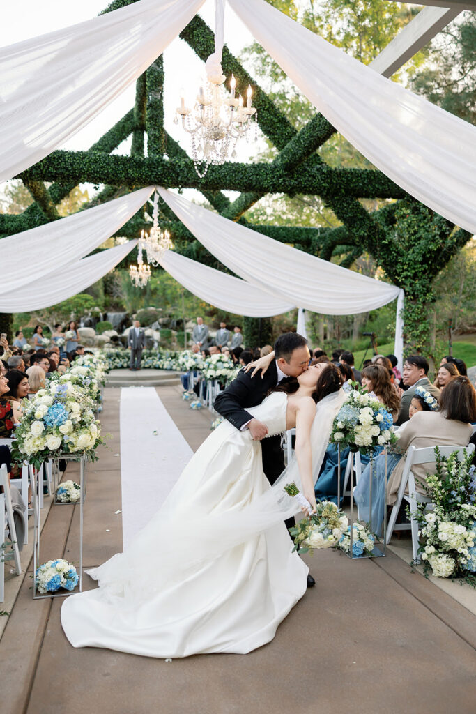 Bride and grooms end of aisle dip kiss during their Coyote Hills Golf Club wedding ceremony.