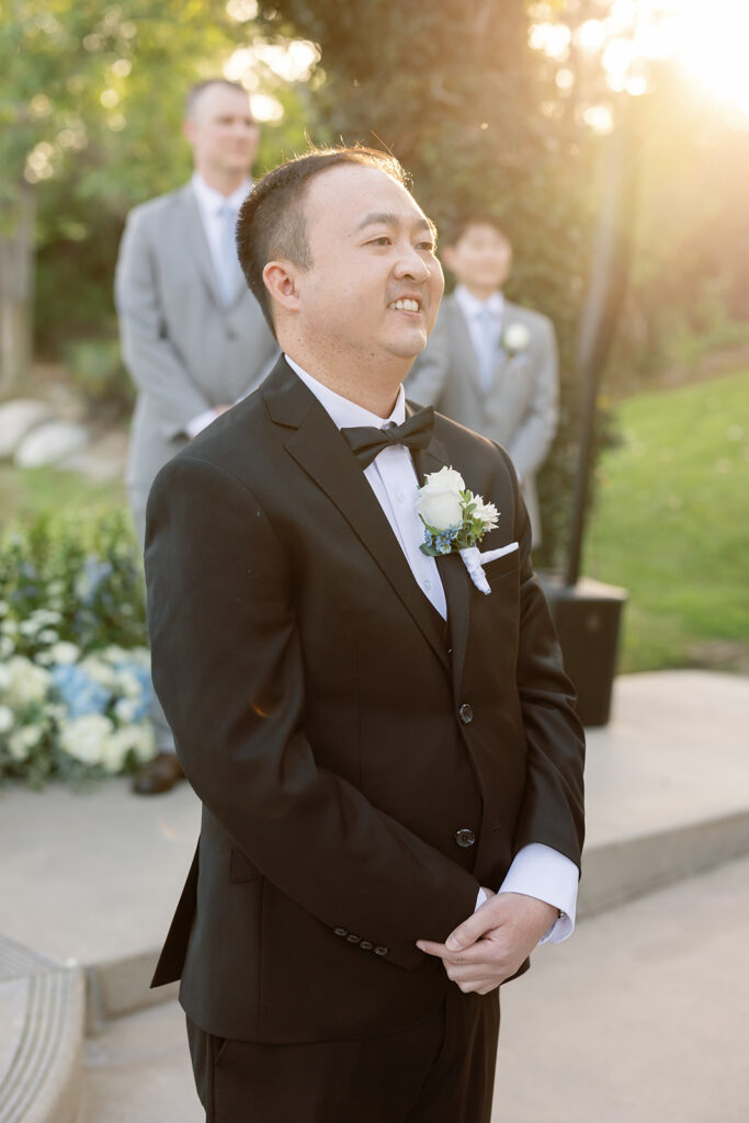 Golden hour photo of the groom smiling as he watches his bride walk down the aisle. 
