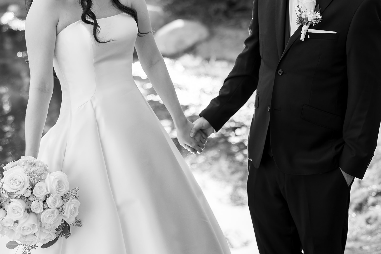Close up black and white shot of a bride and groom holding hands outdoors.