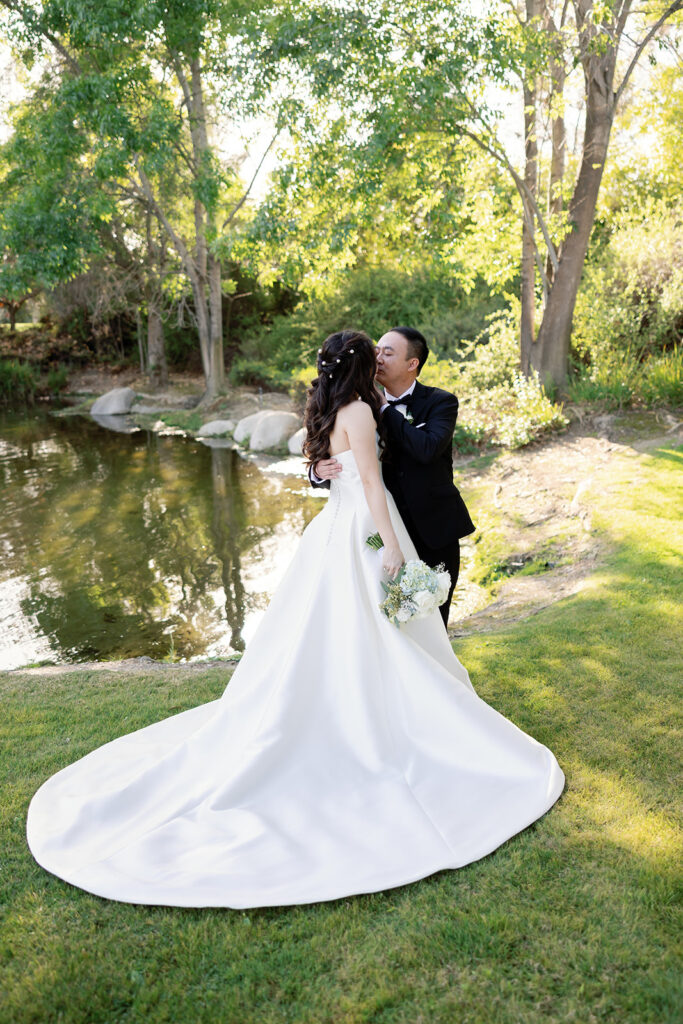 Bride and groom kissing in front of the pond at Coyote Hill Golf Course.