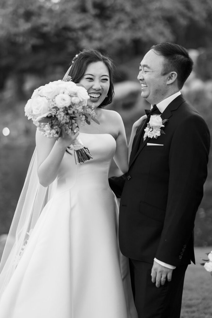 Candid black and white photo of the bride and groom laughing during their portraits.