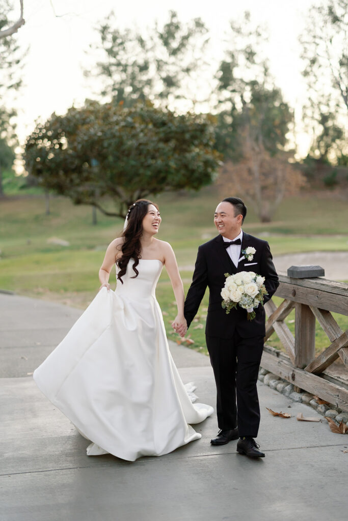 Bride and groom laughing and walking hand in hand during their portraits.