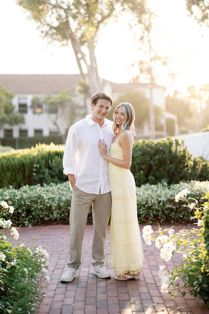 Couple posing for engagement photos at El Encanto in Santa Barbara with golden light and white flowers.