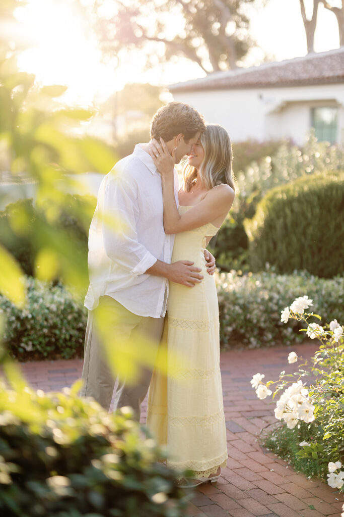 Couple kissing during their El Encanto engagement photos surrounded by greenery and warm sunset light.