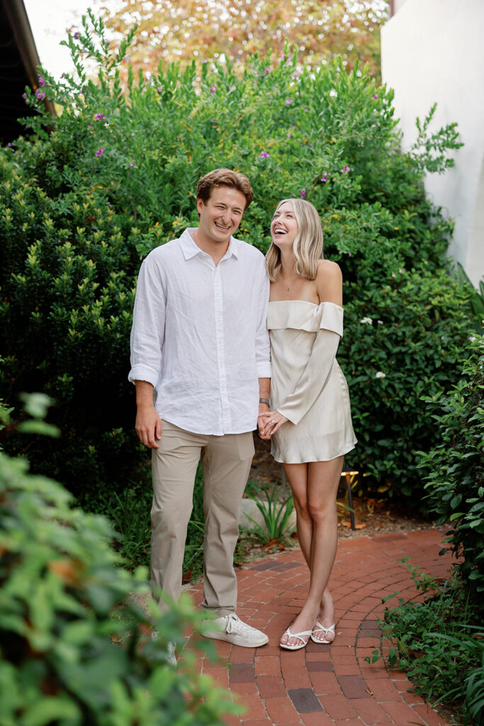 Newly engagement couple laughing together on a garden pathway at El Encanto.