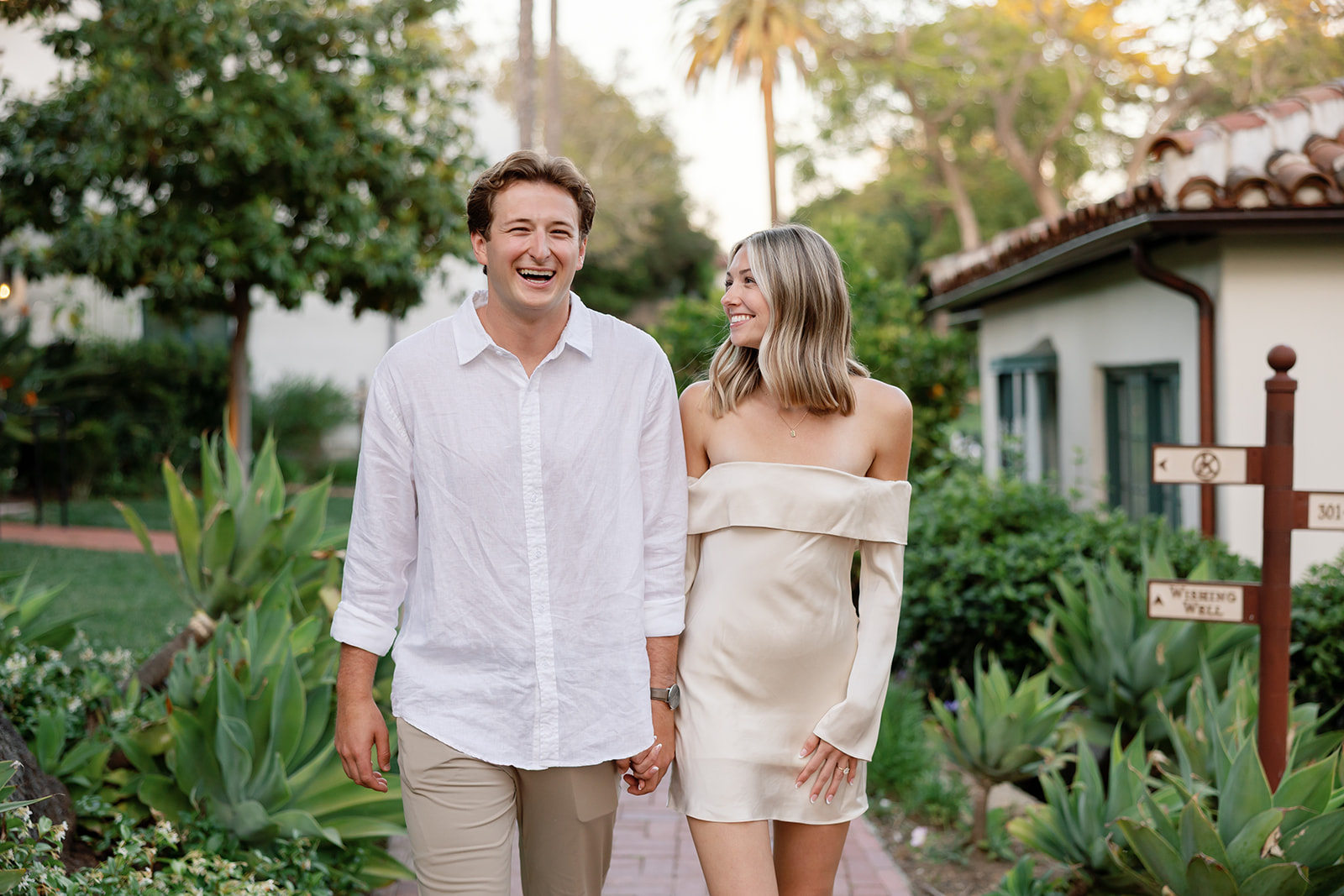Newly engaged couple laughing together on a garden pathway at El Encanto.