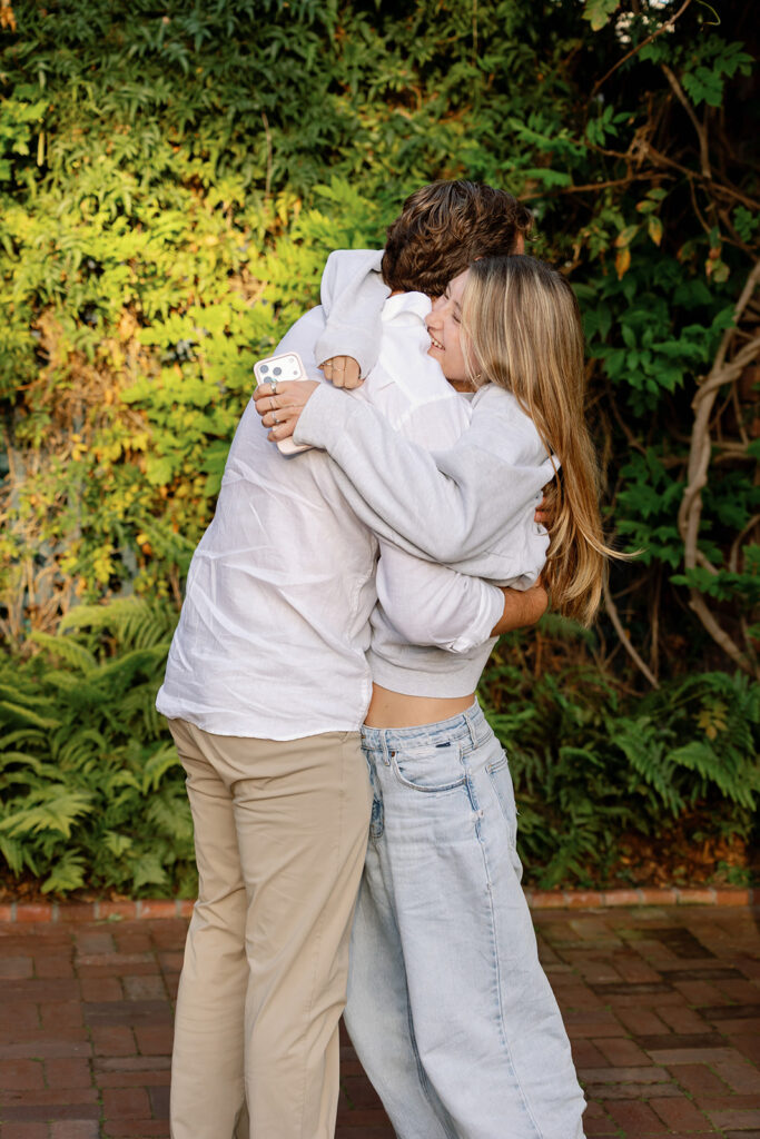 Groom-to-be hugging a sibling after a surprise proposal with family nearby at El Encanto.