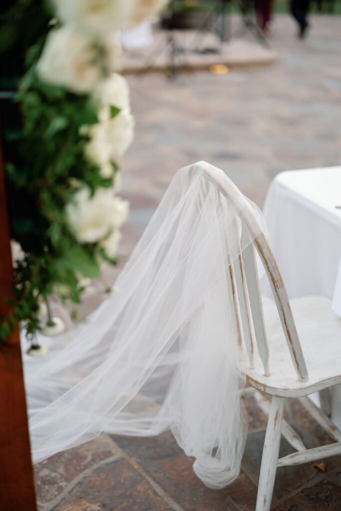 Outdoor reception chair with the brides veil hanging over the back.