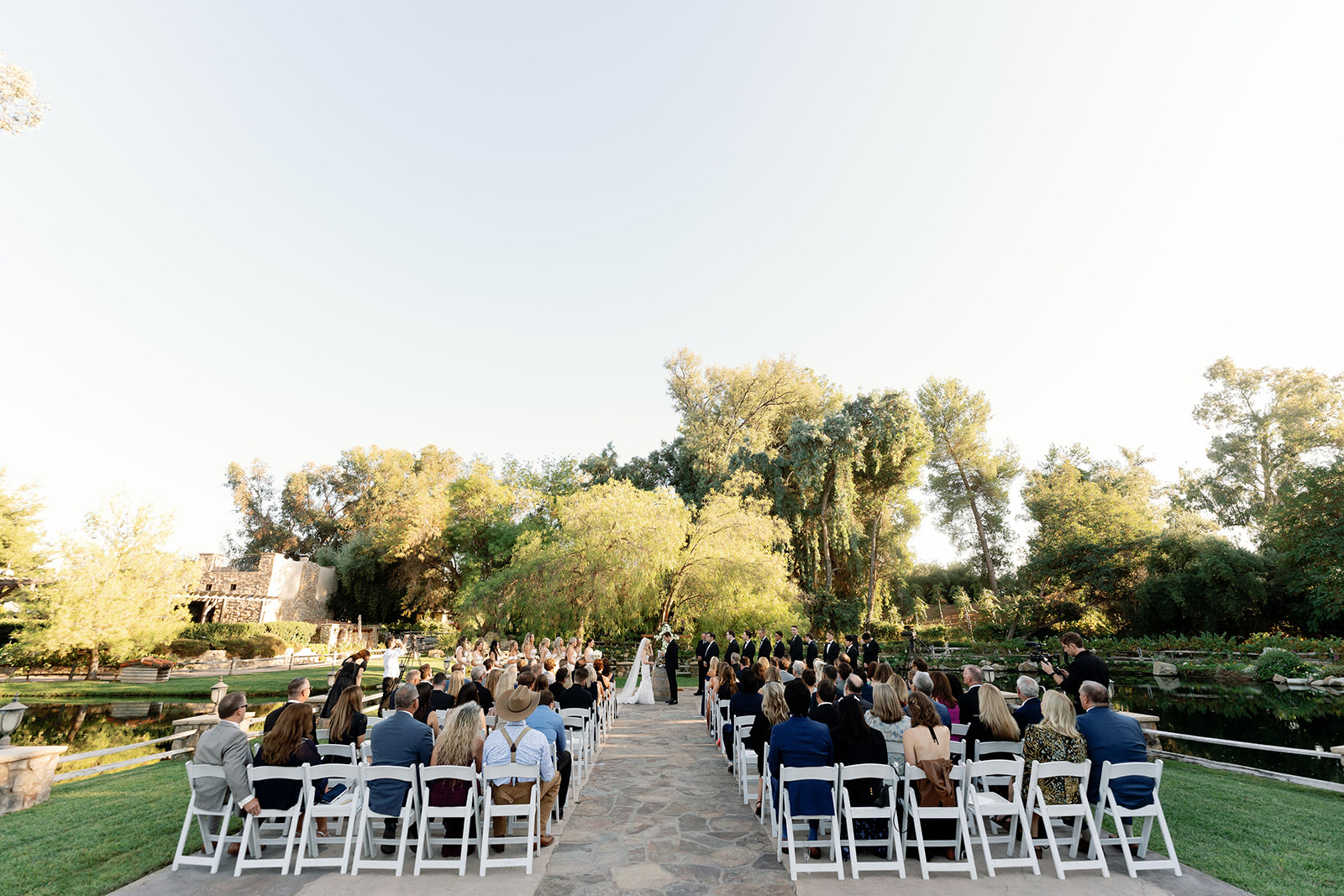 Wide ceremony view with guests, lake, trees, and outdoor ceremony space at Lake Oak Meadows.