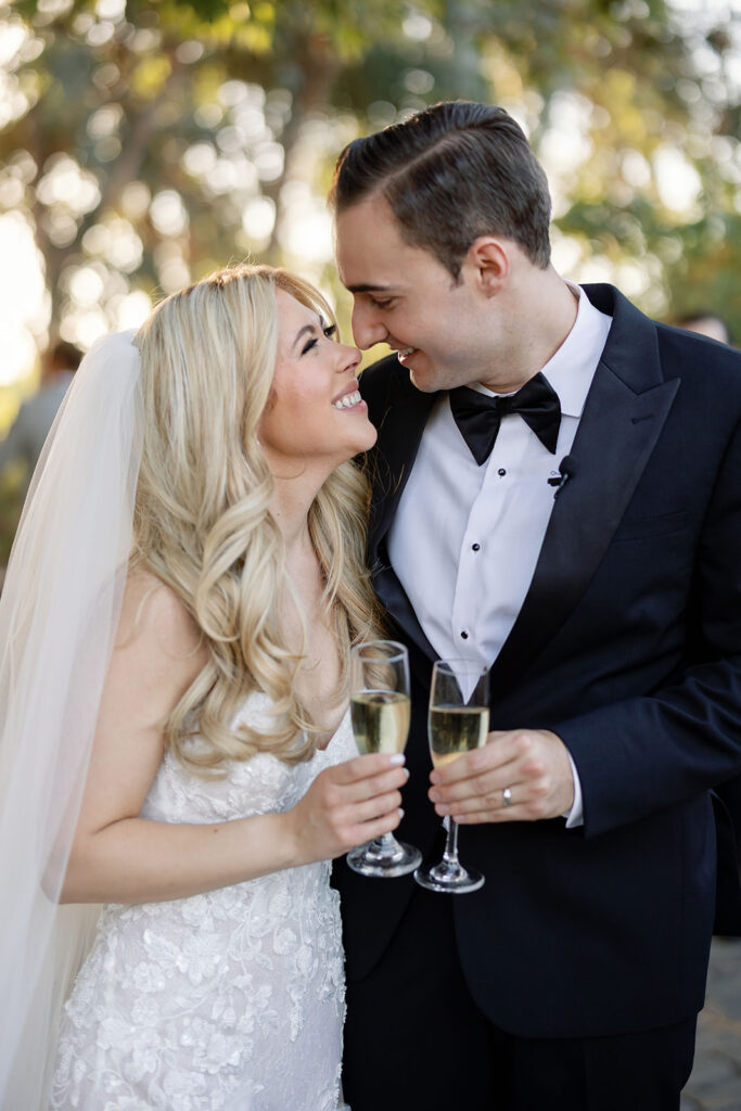 Bride and groom touching noses and holding glasses of champagne.