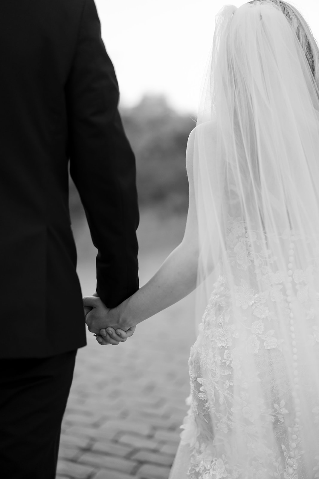 Close up black and white photo of a bride and groom holding hands.