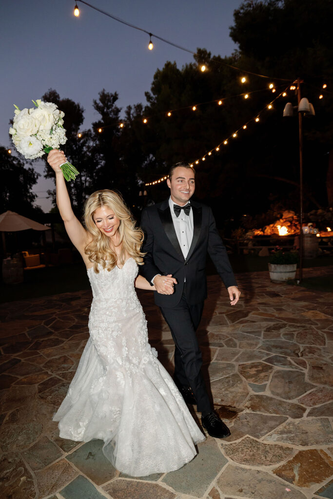Bride and groom walking into their outdoor reception at Lake Oak Meadows under string lights.