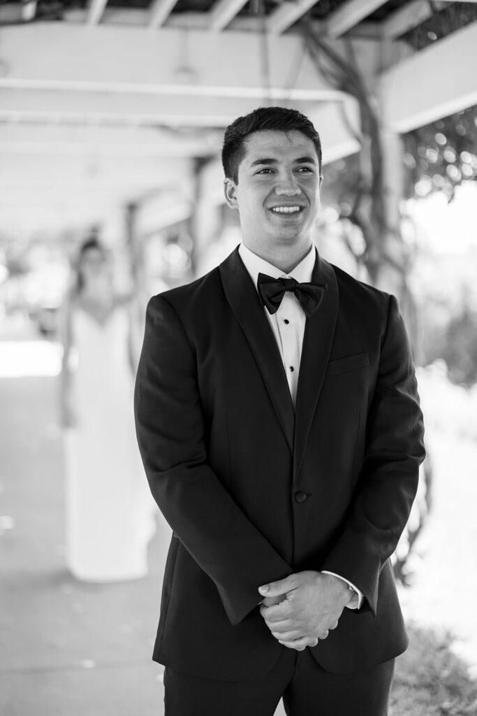 Black and white photo of a bride approaching the groom from behind to share their first look.