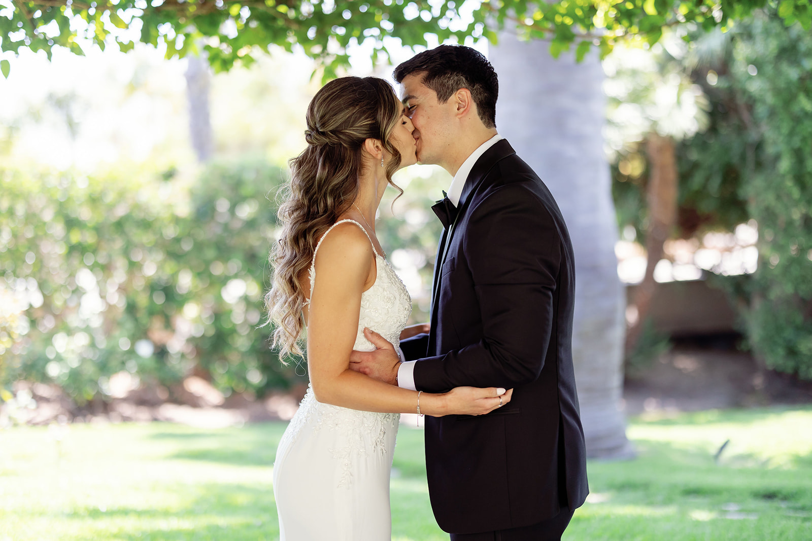 Couple kissing beneath the greenery after their Newport Beach hotel wedding first look.