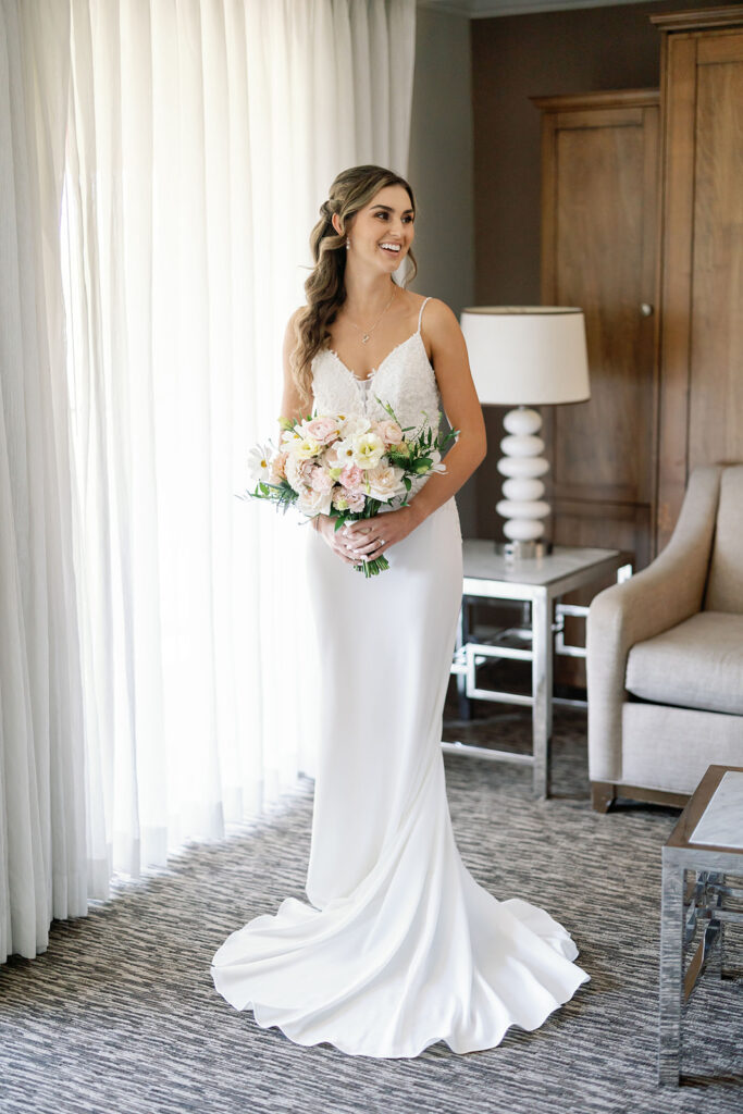 Bride holding a pastel floral bouquet beside a bright hotel room window at Hyatt Regency Newport Beach.