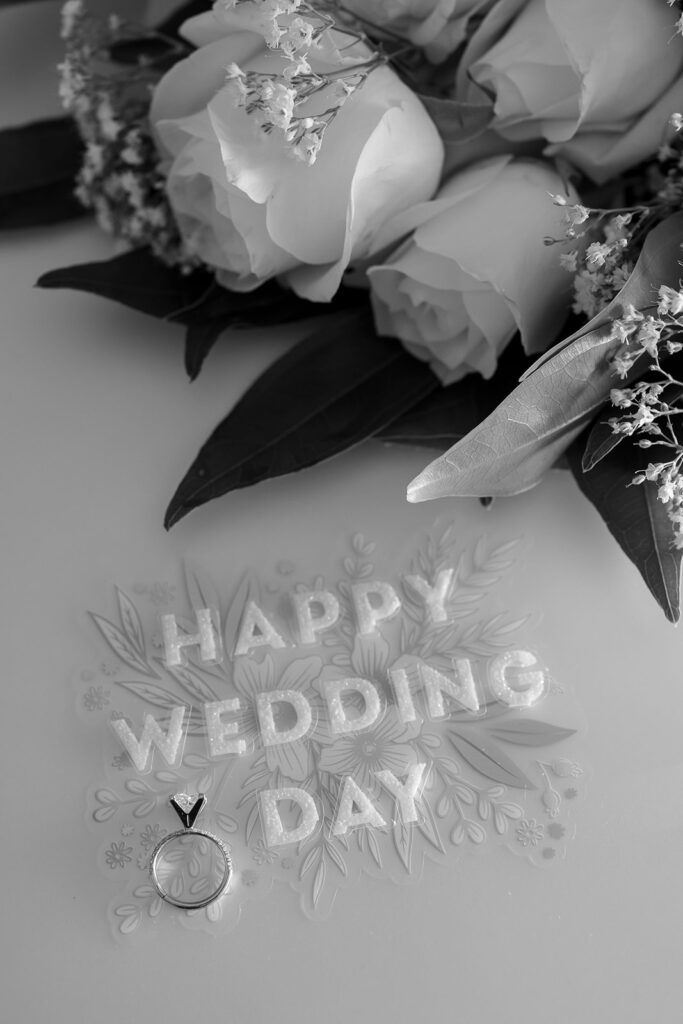 Wedding rings and white roses arranged beside a Happy Wedding Day card.