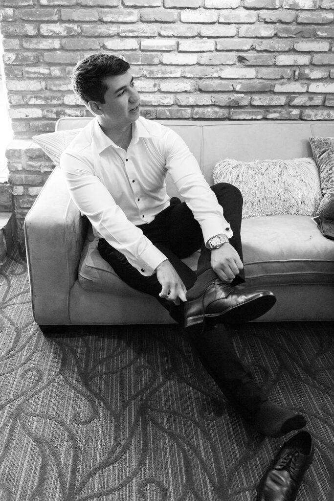 Black and white photo of a groom putting his shoes on. 